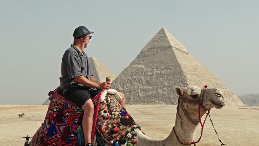Classic Egyptian travel experience: a man sitting atop a camel at the Giza Plateau. The camel is adorned with a vibrant, traditionally patterned saddle.