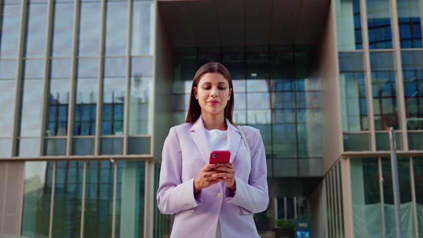 Delighted satisfied adult woman looking at mobile phone screen gesturing yes winning at office building outdoor. Overjoyed excited joyful businesswoman make winner gesture reading bonus or win message