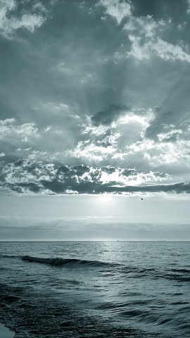 Beautiful seascape. Sea landscape. Ocean scenery. Blue water of calm sea, horizon line, blue sky, white clouds, sun rays shining through clouds. Sunny morning. Sea coast. Natural background Vertical