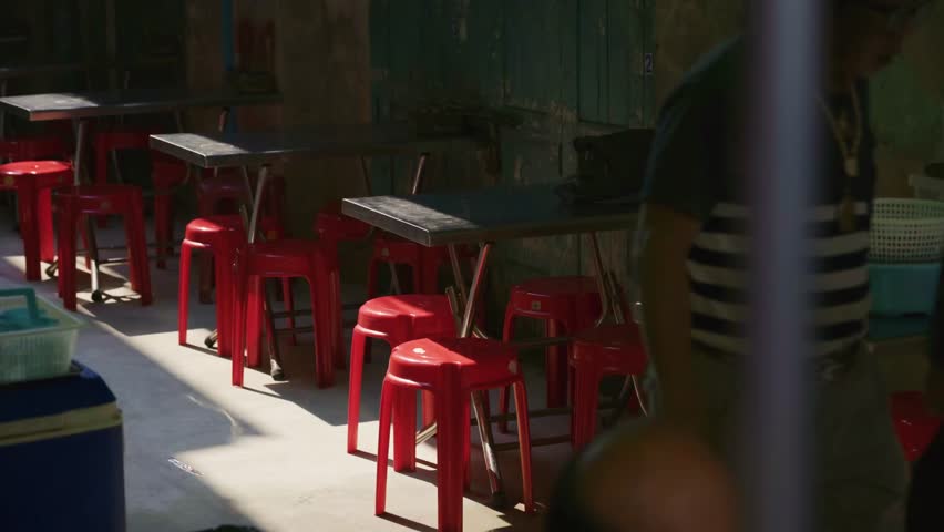 Empty street asian food restaurant patio with red stools and tables in a sunlit alley in Bangkok, Thailand during daytime