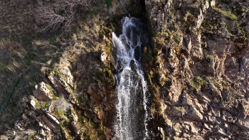 A natural waterfall cascading enthusiastically from steep cliffs. Water droplets sparkling in the sunlight and the peaceful scenery of the wild nature.	