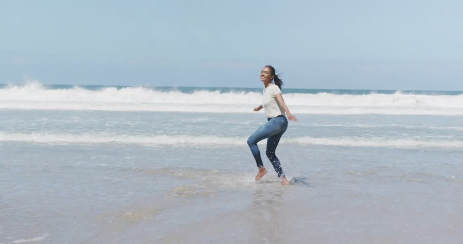 Woman lifting foot as wave touching toes, spinning on beach for health ad with light-leaks floating. Fitness, movement, outdoor, energetic, leisure, scenic, vibrant