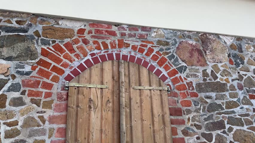 Rustic old wooden shutters in stone wall with brick arch
