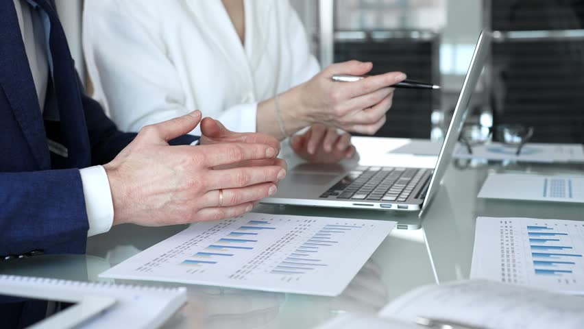 Business professionals examining laptop charts and bar graphs during a modern office meeting, discussing sales performance, market trends, financial analysis and strategy development