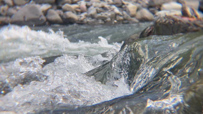 Close-up of Fast Flowing River Water with Splashing Waves and Rocks, A high-angle, close-up shot of crystal clear river water rushing over stones. The image captures the dynamic movement of splashing white foam and the smooth texture of wet river rocks in a natural outdoor setting. Perfect for nature, environment, and travel-themed projects.