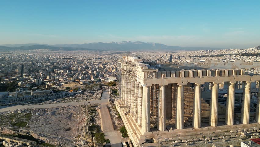 A stunning aerial view of the Acropolis in Athens, overlooking a sprawling urban landscape and distant mountains under a clear blue sky.