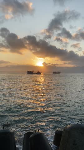 Breathtaking sunset with fiery orange clouds over a calm sea, featuring silhouettes of boats.