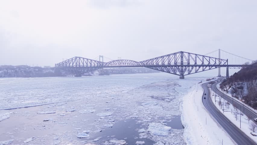 Cinematic winter panorama of Quebec bridges above icy river under dramatic overcast sky.