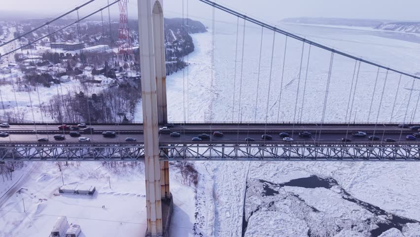 Aerial winter cityscape showing traffic across bridges over icy river in Quebec, captured by drone from high elevation.