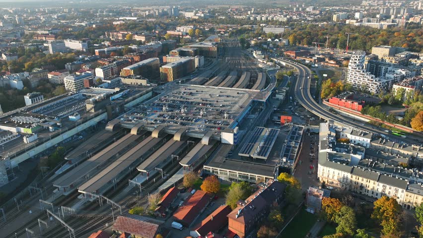 Low altitude drone timelapse video from above of Krakow railway station and transport hub with tracks, platforms and surrounding city in autumn daylight