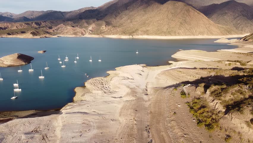 Aerial shot reveals a serene yet arid landscape in Potrerillos, Mendoza. Mountains surround a partially dry lake. Ideal for travel, nature