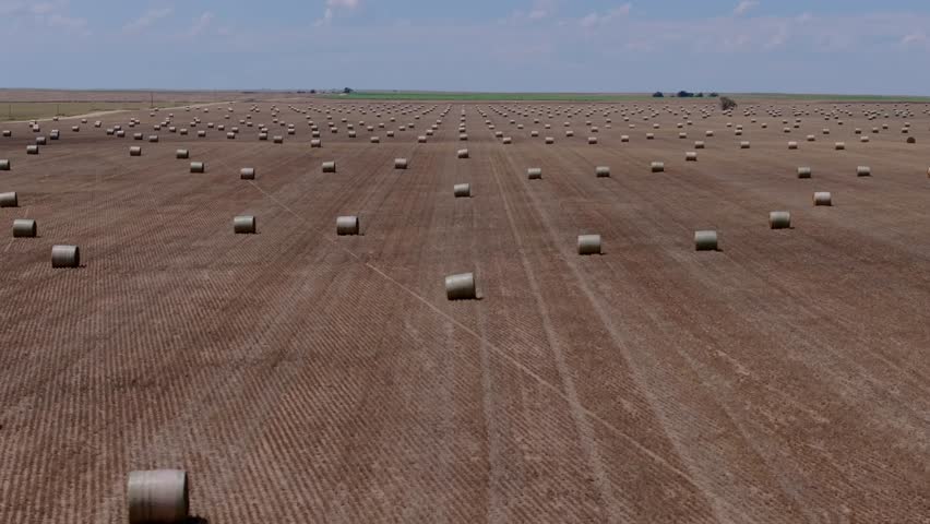 Aerial establishing evenly spaced hay bales across harvested Kansas field, agriculture perfect rows and tracks