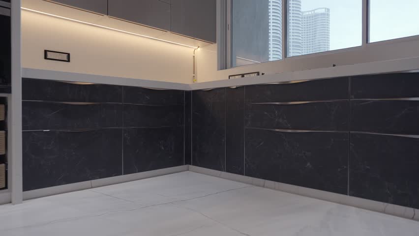 Modern kitchen with dark lower cabinets, glossy upper cupboards, built in gas stove, and a wide window showing city skyscrapers.