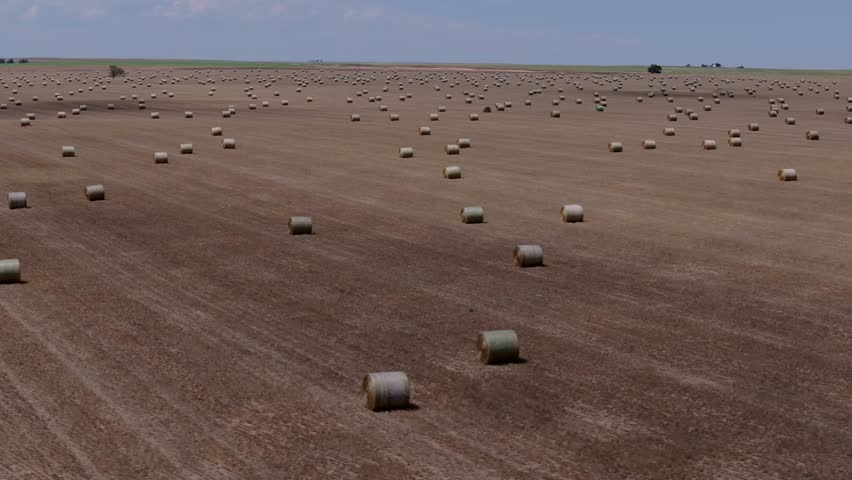 Flat Kansas farmland with scattered hay bales under wide sky, aerial tracking right, backdrop