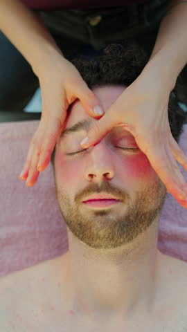 Man with closed eyes enjoying a professional head and face massage, promoting wellness and stress relief at a spa.