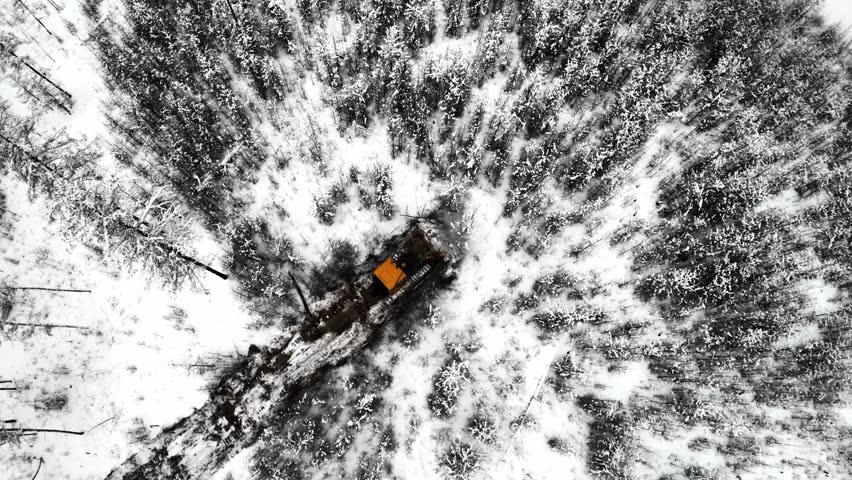 A yellow snow-clearing vehicle pushes through deep snow in a forested area, creating a cleared path. view from the top