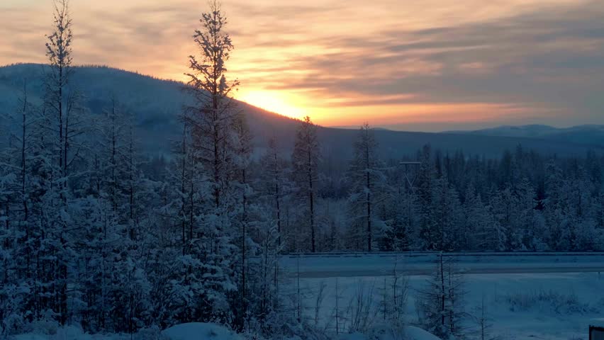 A snowy forest landscape with a road and mountains at sunset, promoting winter travel and adventure.