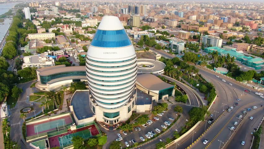 Aerial drone view of Corinthia Hotel in Khartoum, Sudan, showing modern landmark architecture, surrounding roads, city buildings, urban layout, and busy metropolitan environment in daylight