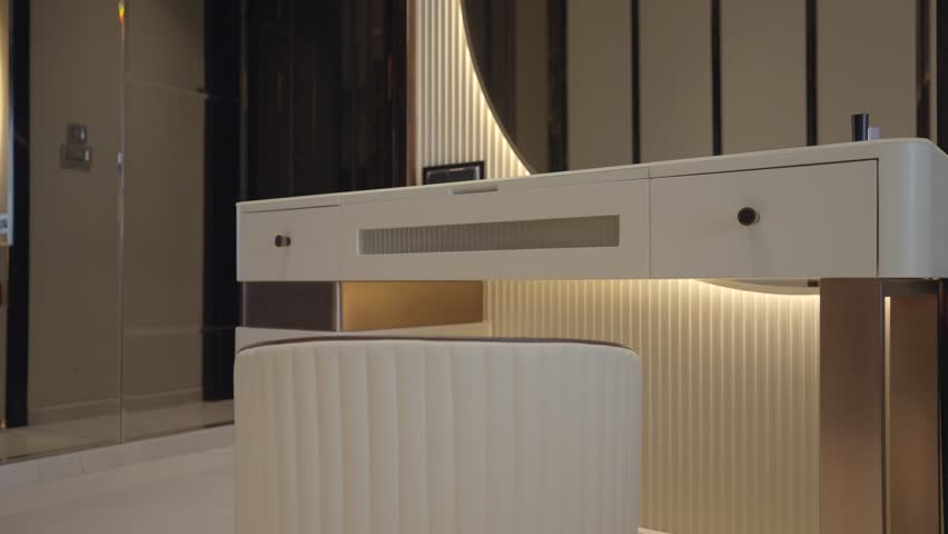 White vanity table with metallic legs, ribbed backdrop, warm underlighting, and round mirror