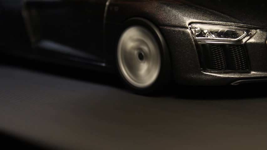 A closeup of a gray scale toy super car running on a treadmill simulating a roadtrip