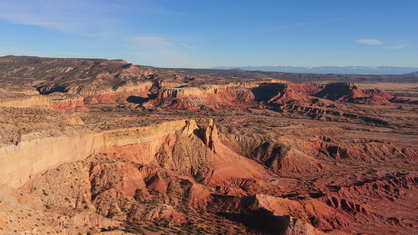 Eroded white sandstone cliffs and spires tower over a high desert landscape in the American Southwest. The arid environment features red rock formations and dry brush under a clear blue sky.