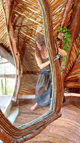 Woman standing in front of a mirror inside a rustic building. A woman stands by a mirror inside a building made of wood and natural materials in Mexico.