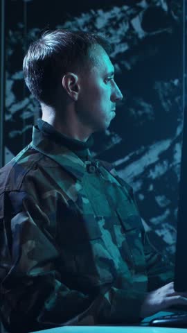 Soldier in a dimly lit military control room, intensely focused on multiple computer screens displaying crucial operational drone data.