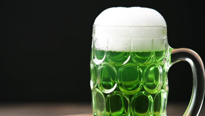 Green beer mug with foam for St. Patrick’s Day on wooden table and black background