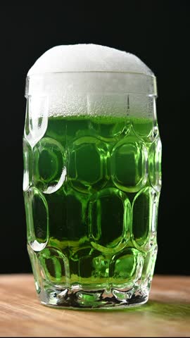 Green beer mug with foam for St. Patrick’s Day on wooden table and black background