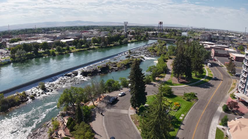 An aerial view of Idaho Falls running through with bridges, adjacent roads, and green trees along its banks.
