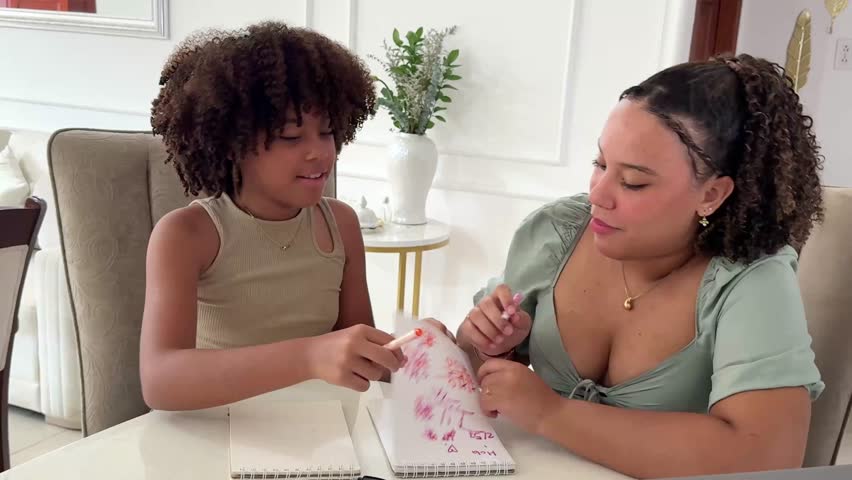 An older sister passes on her knowledge while teaching her younger sister to draw in a notebook at home.