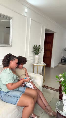 Caring older sister helps her younger sibling with her homework, sharing knowledge in the living room