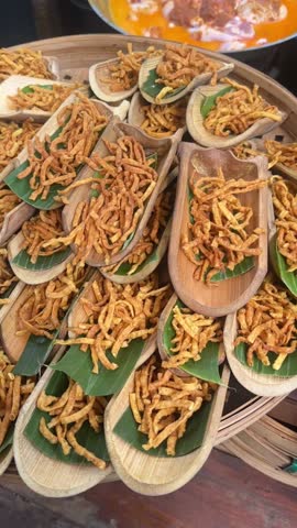 Vertical video of Thai Khao Soi crispy noodles arranged in bamboo cups with banana leaves, golden fried texture presented as traditional street food at local market