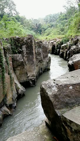 Peaceful Waters Amidst Rocky Cliffs 

A stream cuts a path through a rocky gorge, surrounded by vibrant green plant life. Capturing the raw, untamed beauty of nature.