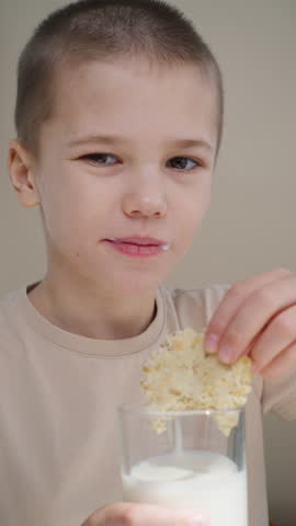 Little boy dips oatmeal cookies into a glass of fresh yogurt.