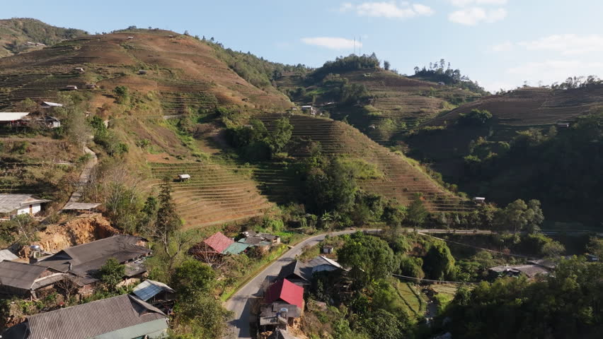 Panoramic aerial view of Vietnam terraced rice fields at Mui Giay, Mu Cang Chai, Yen Bai, with mountain slopes, village roofs and winding road in clear daylight.