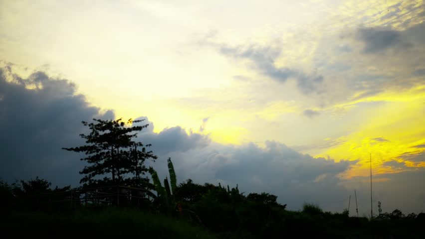 Cloudy evening sky with warm sunset light glowing behind clouds.silhouette of trees under dramatic sky, creating calm and atmospheric natural scenery