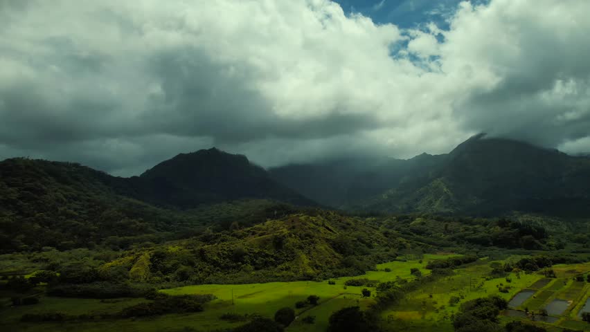 Drone aerial above tropical fields and clouded peaks of Kauai