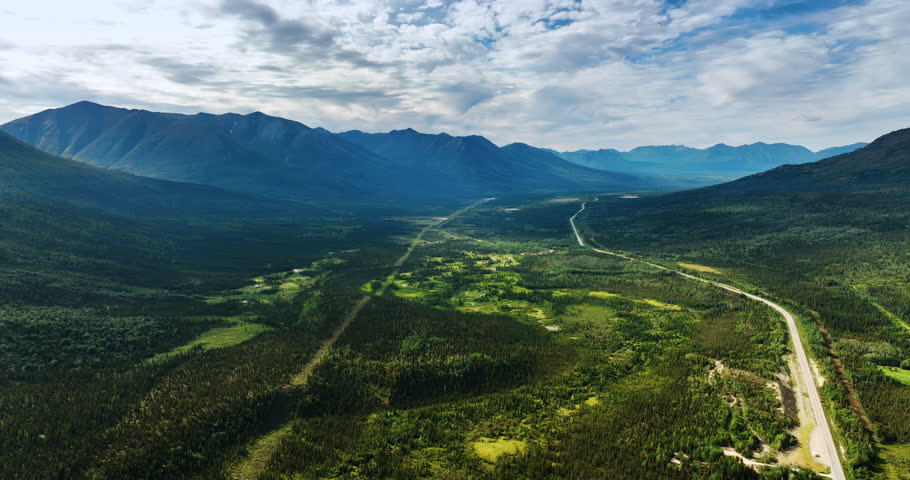 Spectacular vast valley among the stunning mountains. A road crosses the landscape. Aerial perspective on the nature of Alaska.