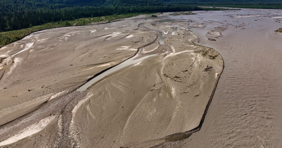 Dried up river sandy bottom. Footage from drone. Vast green woods grow around. Spectacular mountains of Alaska at backdrop.