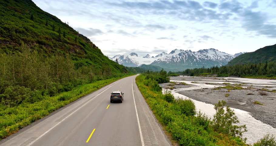 Following a car moving by the road along the delta of the dried up river. Jaw-dropping view of the mountains in Alaska from drone.