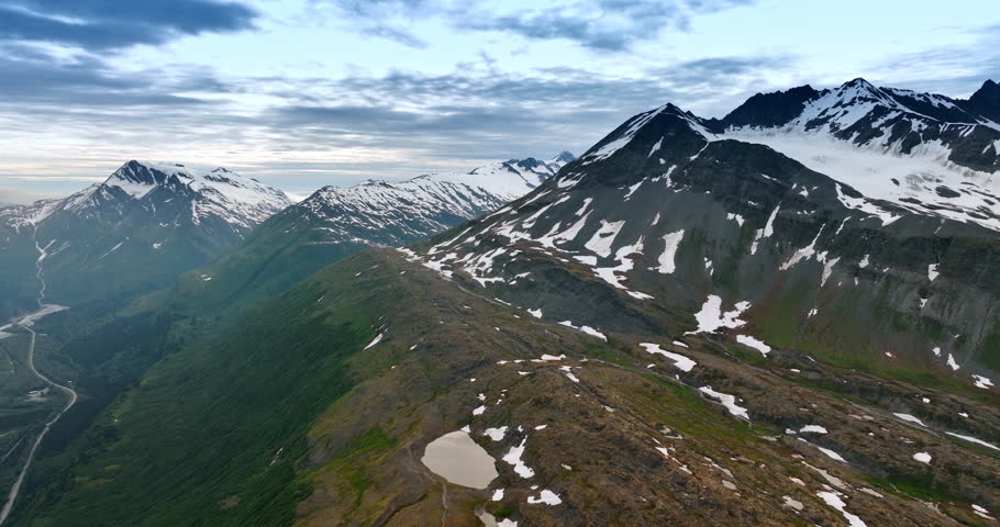 Spectacular mountains with little snow on the slopes. Drone footage over the rocks under the overcast sky. Alaska wilderness.