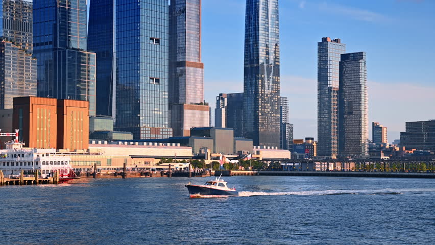 Little motorboat travels by the riverscape in New York, USA. Stunning high-rises of metropolis at backdrop.