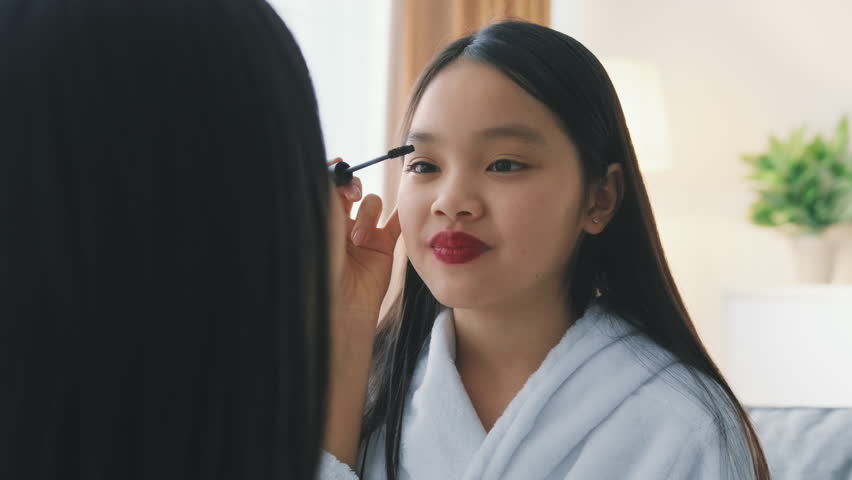 Young Girl Applying Mascara in a Bright Room While Looking in a Mirror
