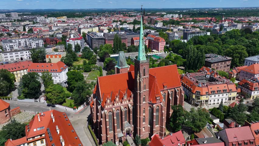 Panoramic Aerial Orbit of Wrocław Cathedral and Historic Ostrów Tumski. A breathtaking aerial orbit centering on the towering green spires of the Cathedral of St. John the Baptist in Wrocław, Poland. The footage provides a 360-degree perspective of Ostrów Tumski (Cathedral Island), the city