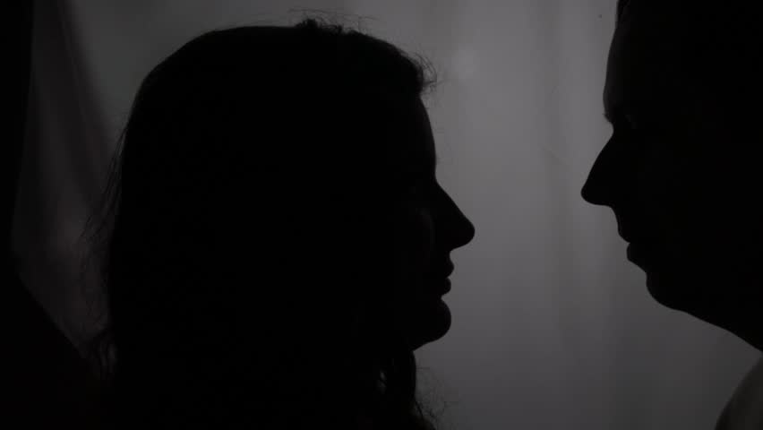 Silhouette on the window background. The newlyweds stand at the window in profile. The bride and groom near a bright window. Tender moment. Romantic couple silhouette near the window.