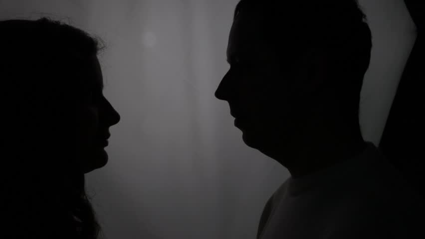 Silhouette on the window background. The newlyweds stand at the window in profile. The bride and groom near a bright window. Tender moment. Romantic couple silhouette near the window.