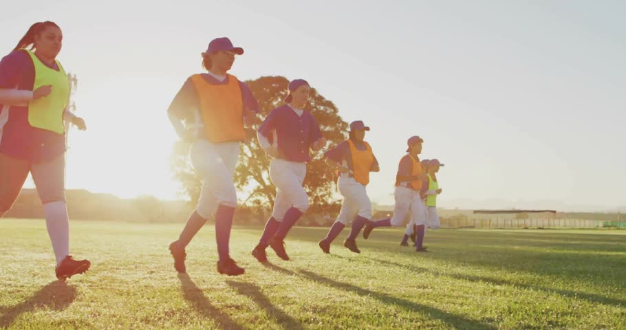 Seven softball players jogging on field, lowering into crouch then sprinting for power training. Athletes, teamwork, training, outdoor, energetic, athleticism, competition