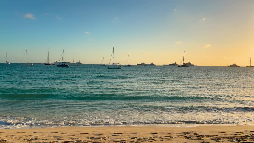 A view of the Caribbean Sea with moored sailboats in the distance from the island's sandy beach during a picturesque sunset. Island Saint Martin, the Caribbean.