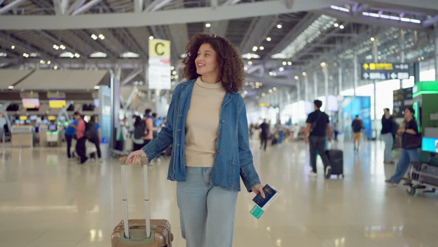 Latino woman walking through airport terminal toward the boarding gate. Attractive beautiful female tourist traveler feel happy and excited while preparing to fly abroad for holiday vacation trip.